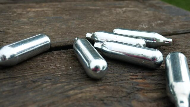 Dangerous chrome nitrous oxide laughing gas drug cartridges on wooden park table pan closeup right