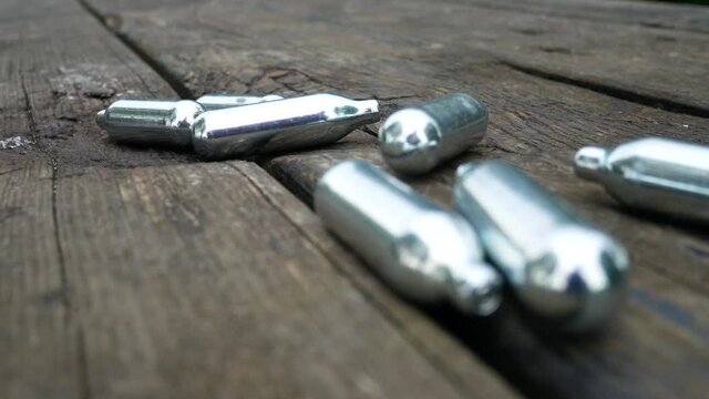 Multiple chrome nitrous oxide laughing gas drug cylinders closeup dolly right across wood park bench