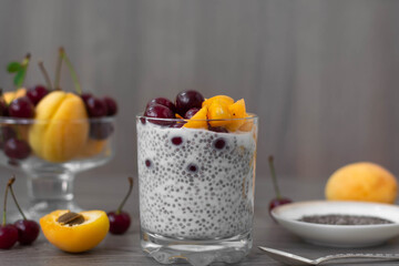 Healthy vegan breakfast of chia seed pudding topped with fresh apricots and cherries. More fruit and a vintage silver spoon in the wooden background. Rustic and dark aesthetic
