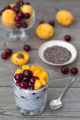 Healthy vegan breakfast of chia seed pudding topped with fresh apricots and cherries. More fruit and a vintage silver spoon in the wooden background. Rustic and dark aesthetic