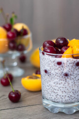 Healthy vegan breakfast of chia seed pudding topped with fresh apricots and cherries. More fruit and a vintage silver spoon in the wooden background. Rustic and dark aesthetic