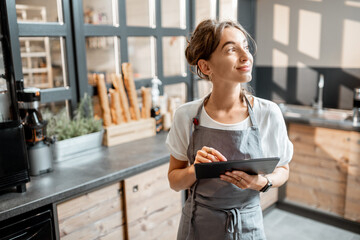 Young saleswoman working with a digital tablet at the counter of cafe or confectionary shop. Concept of a small business and technologies in the field of services