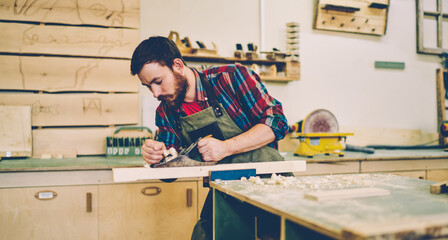 Caucasian man spending time for wood hobby making construction in garage with equipment, handsome male carpenter owner of restoration manufacture working with tools and repair details indoors
