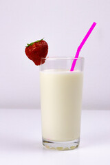 glass of milk with strawberries and a tube on a white background
