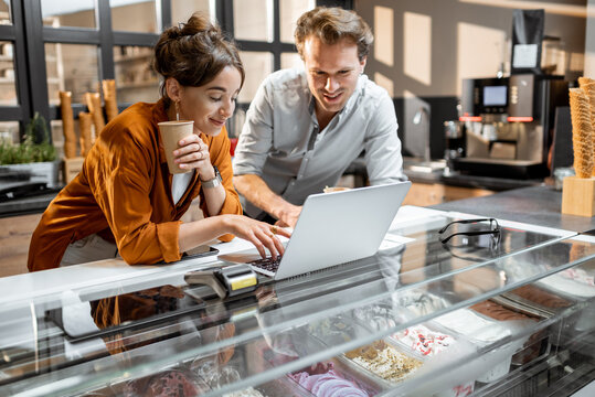 Two young managers or shop owners having some discussion working on a laptop at the counter of the shop or cafe. Small business management concept
