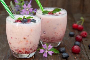 Berries smoothies in two glasses with straws on wooden table. Fresh homemade smoothie with blueberries, raspberries and sour cherries.