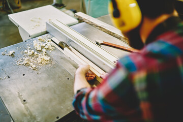 Cropped male student using circular on carpentry courses learning how to making wooden plank, rear view of skilled craftsman in headphones for safety working on professional equipment with timber.