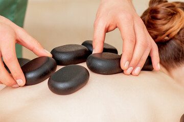 Obraz na płótnie Canvas Male hands laying large new oval black hot stones for back massage on female back in spa salon
