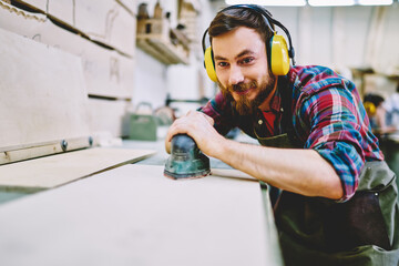 Cheerful caucasian male in protective equipment making polish with sander satisfied with his...