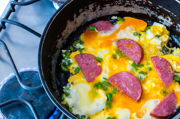 scrambled eggs with ham, vegetables and cheese in a pan is cooked on the stove