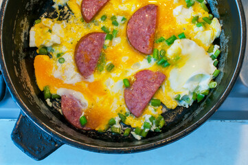 scrambled eggs with ham, vegetables and cheese in a pan is cooked on the stove