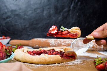 homemade strawberry Galette with fresh ripe strawberries on a dark background, top view. cut cake, a piece of Galette on a knife