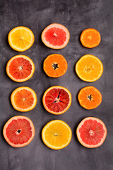 Multi-colored layout of circles of red and orange oranges, tangerines and grapefruit on a gray background, top view.