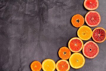 Circles of red and orange oranges, tangerines and grapefruit on a dark gray background from the side. Delicious and healthy food concept.