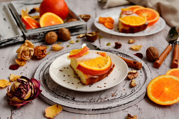 Rustic still life of homemade pie with oranges and walnuts on white plates on a light old table. Close-up