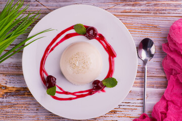Panna cotta, white pudding with berries, red fruit sauce on a background of flowers and a wooden...