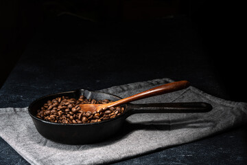 Freshly roasted coffee beans in a cast iron skillet. Linen napkin. A natural stone. Dark background.