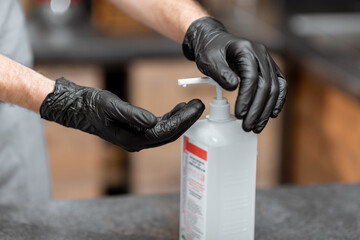Seller in black gloves disinfecting hands while working in a grocery store or cafe, close-up view. Concept of a new rules for business during a pandemic