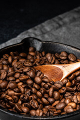 Freshly roasted coffee beans in a cast iron skillet. Linen napkin. A natural stone. Dark background.