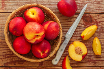 Nectarine. Ripe juicy organic nectarines (peaches) in a wicker basket. Whole and sliced fruit on a wooden table. Selective focus, top view, copy space