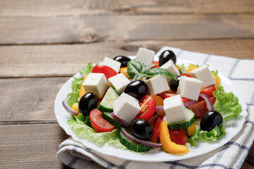 Greek salad with cheese and fresh vegetables on wooden background.