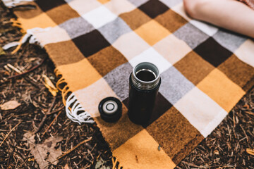 Black camping thermo mug on a plaid while hiking in the forest, outdoor recreation concept.