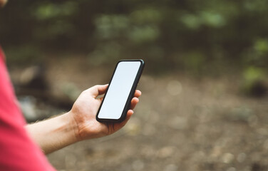 A man holds a smartphone with a white screen in a forest clearing while hiking.