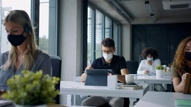 Young people with face masks back at work or school in office after lockdown.