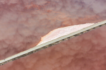 Clouds reflected on the red-algae rich Lake Magadi surface crossed by a causeway, Great Rift Valley, Kenya.