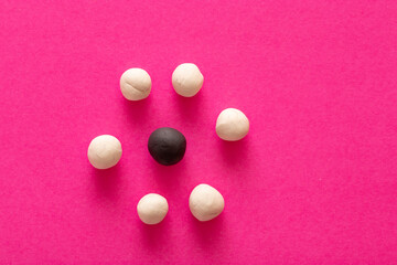 Multiple white balls surrounding a single black one on pink vibrant background. Concepts of racism and intolerance in women