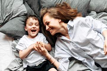 Mom and little cute child have fun at home. Young mom and toddler son lie on the bed and laughing....