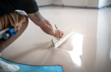 Handwerker verteilt die frische Ausgleichsmasse mit der Rakel 