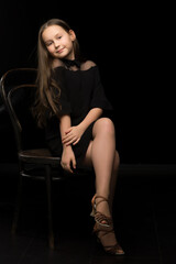 Naklejka premium Portrait of a little girl sitting on an old Viennese chair, black background.