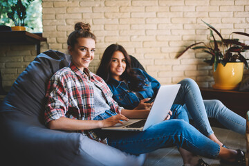 Portrait of smiling friends studying at laptop device with free wireless internet connection in...