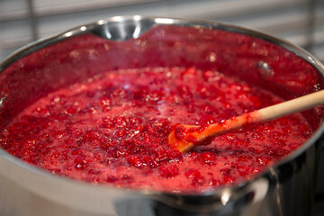 Cooking raspberry jam in a saucepan. Wooden spoon in a saucepan.