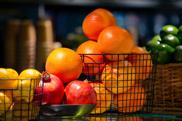 Variety of citrus fruit and garnets in black metal baskets on a glass shelf in cafe.