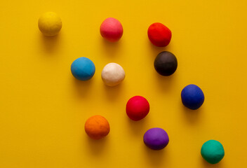 Many different colored plasticine balls on a yellow background. Colorful top down view, hand rolled childrens toys