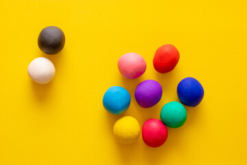 Black and white plasticine ball staying together, separated from a group of other colorful balls. Concepts of difference, racism, social issues and unacceptance