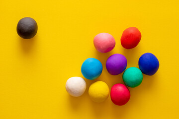 Black plasticine ball excluded from other balls in many colors. Concepts of discrimination, unacceptance, racism and diversity