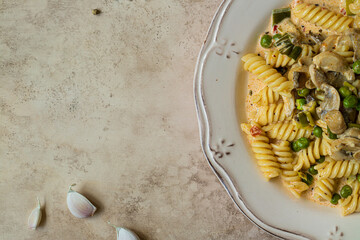 fusilli with peas, tomatoes and mushrooms on beige background. top view close up. copy space