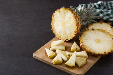 Fresh pineapple slices on cutting board and black stone background. Copy space