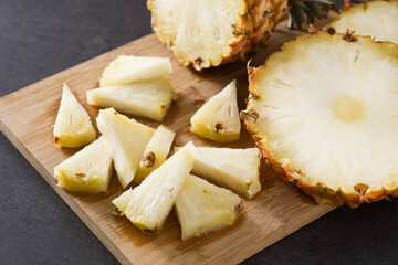 Fresh pineapple slices on cutting board and black stone background