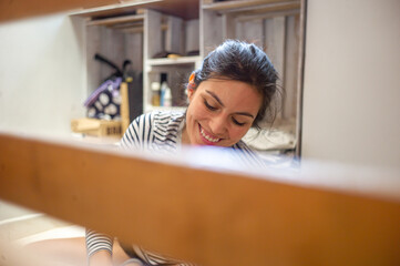 Young Attractive Hispanic Woman in Black and White Stripes Long Sleeve Shirt Paints a Wooden Pallet in White Smiling at Home