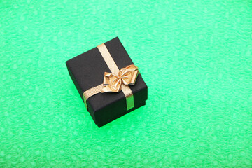 Black gift box for jewelry decorated with a gold ribbon. Bright green background.