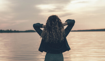 Fototapeta premium A girl stands with her back and looks at the sea, a girl at sunset near the sea