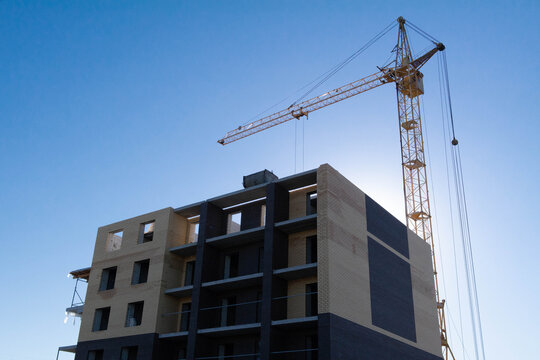 Brick building under construction and a high-rise crane against a blue sky. Construction of an office, house. A shot against the sun for an advertising company in real estate industry and business.