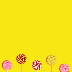 Creative Flat lay with with sweet round candy lollypops with stripes on stick on yellow paper...