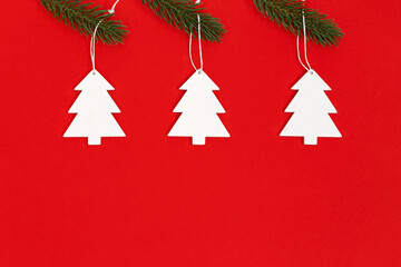 Fototapeta na wymiar New years Christmas tree from white wood hanging on pine branch on red background. Christmas greeting card. Minimal style.