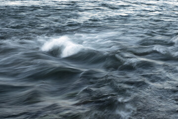 The stream of water, blurred view. Powerful water flow with breakers on the sea