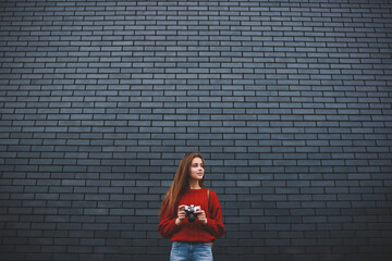 Attractive casually dressed hipster girl strolling with vintage camera enjoying free time outdoors standing on urban setting brick wall copy space area for advertising content or text messages